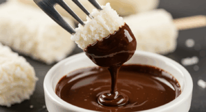Bombom Prestígio low carb sendo banhado em chocolate derretido.